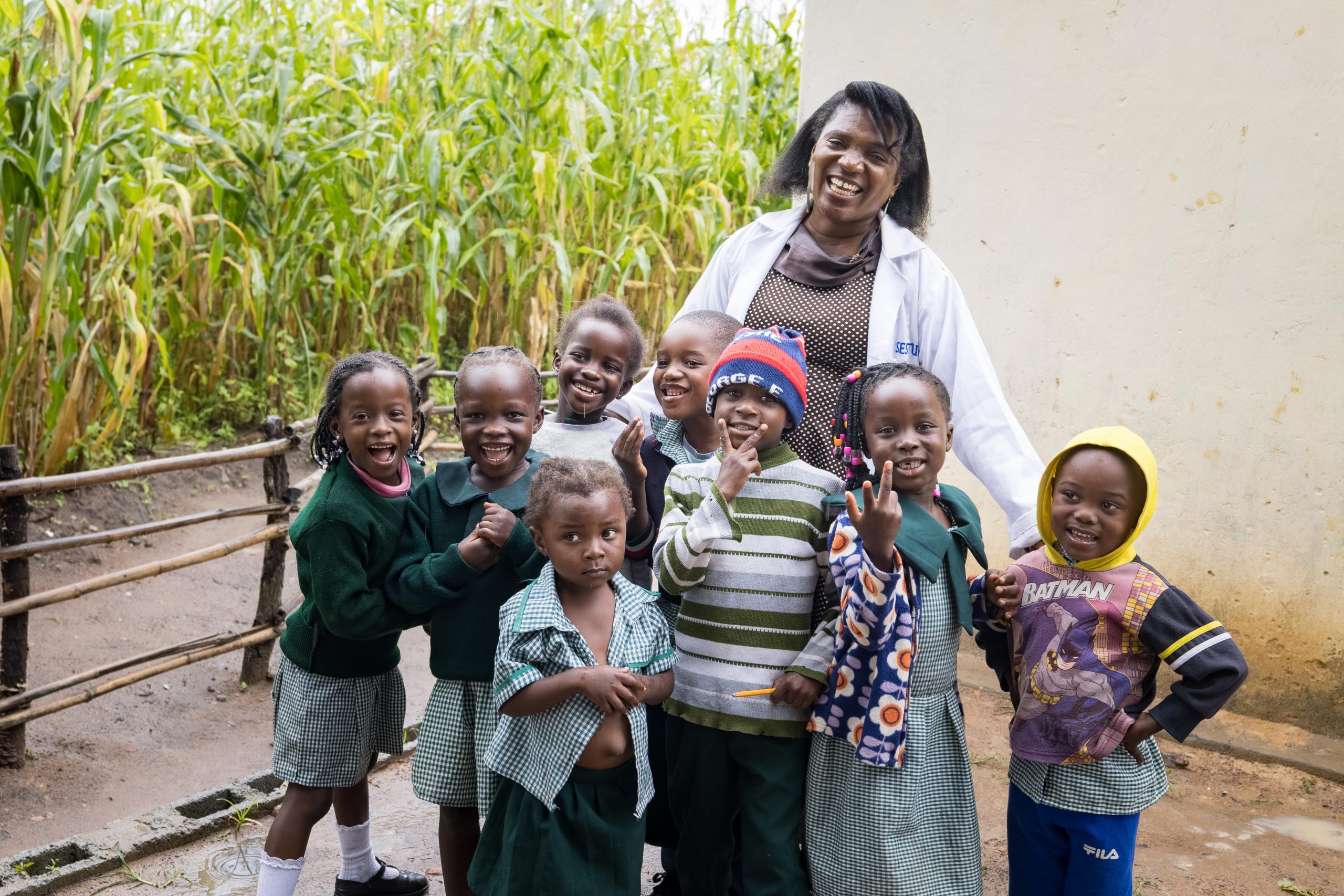 A woman smiles with eight preschool students outside a building.